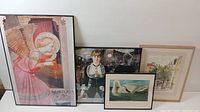 Four framed art prints leaning against wall, showing distinct artworks including angelic figure and Manet reproduction