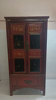 Full front view of tall Asian lacquer cupboard with red and black painted floral and bird motifs on doors and lower panel.