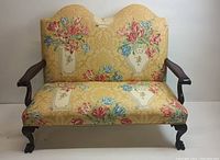 Full front view of a camelback sofa upholstered with yellow damask fabric featuring floral bouquets in vases. Shows overall design and fabric condition.