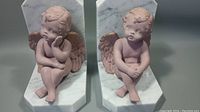 Pair of marble and chalkware cherub bookends shown individually in neutral light background