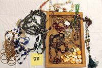 Top view of assorted costume jewelry arranged on a fabric, including necklaces with blue, gold, amber, and shell-like beads.