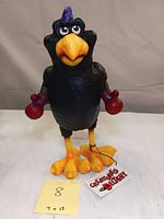 Front view of the Creatures of Delight rubber composite black bird sculpture wearing red boxing gloves, with tag and measuring note (7 x 13).