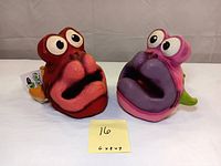 Two Creatures of Delight rubber composite fish sculptures, one red and one pink, positioned side-by-side with a size note showing 6x8x7.