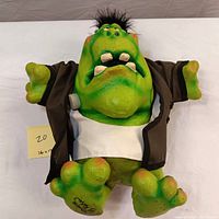 Front view of the green Frankenstein sculpture showing the large feet, open mouth with teeth, brown jacket, and signature on foot.