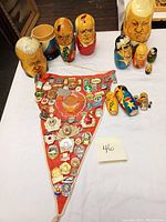 Photo showing a collection of hand-painted Russian nesting dolls and a red triangular pennant densely covered with pins of Soviet and Russian themes.