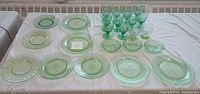 Full view of the entire vintage green glassware collection laid out on a table showing plates, stem glasses, and bowls.