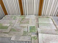 Overview of multiple folded paper maps spread over two tables, showing various regions mostly from California and Nevada with colored terrain details.