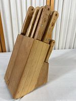 Wooden knife block holding 7 knives visible, natural wood finish with angled slots for knives.