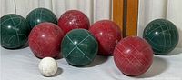 Photo of 8 bocce balls: 4 red and 4 green with 1 small white pallino ball at the front. Balls show some wear.