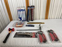 Full layout of tools including saw blades, socket sets, rubber mallet, clamps, wrenches, utility knife, hacksaw, and measuring ruler laid out on white surface.