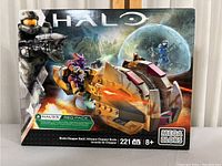 Front view of sealed Mega Bloks Halo Brute Chopper Raid box showing detailed vehicle build and blurred background with mini-figures in battle scene.