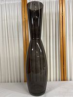 Full view of the tall clear smoke-colored glass vase showing its shape and size in front of white curtains.