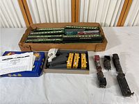 Overview photo showing the collection of various model train pieces organized in boxes and foam inserts on a white table.