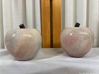 Two stone apples side by side on a white surface with a wood and fabric background.