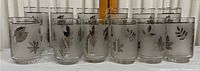 Full set of twelve drinking glasses arranged with two different sizes and reflective chrome leaf decoration visible.