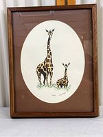Full framed print showing two giraffes on an oval white background with a reddish-brown mat and medium brown wooden frame.
