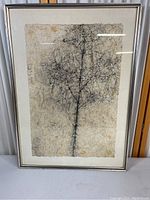 Full view of framed abstract print with black linear tree shapes on textured white and yellow background.