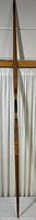 Full length view of a wooden archery bow standing vertically showing its natural wood finish and overall condition.