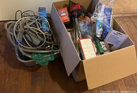 Box and plastic container with assorted tropical fish care supplies including food, medication, filters, nets, siphons, scrapers and multiple accessories mostly in retail packaging.