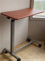 Full view of the bedside table showing adjustable height metal base with caster wheels and wood grain laminate top.