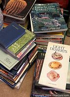Stacks of used books including a gardening book titled 'Four Season Gardening' and a cookbook 'Light Desserts'. Other books are in the pile but titles are partially visible or obscured.