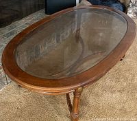 Top view of oval coffee table showing clear safety glass top in brown wood frame.