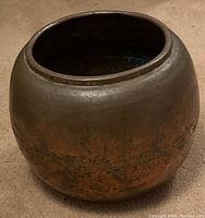 Full view of rounded vintage copper pot showing overall weathered surface and open top.