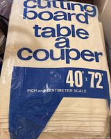 Plastic-wrapped fabric cutting board cover with printed instructions and dimensions visible on packaging.