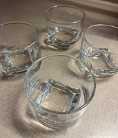 Four clear whiskey glasses shown from a top angle, displaying thick square bases and cylindrical shape.