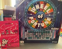 Photo showing the boxed Wheel of Fortune board game and Simon's Cat card game boxes side by side.