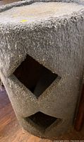 Photo of barrel shaped kitty condo covered with worn blue carpet showing two diamond-shaped entrances.