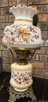 Side view of the vintage electric table lamp with floral glass shade and brass base against a brick background.