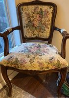 Full view of Louis XV style chair with floral tapestry upholstery on seat and backrest, showing dark carved wood arms and legs.