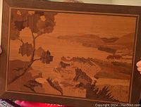 Full view of framed marquetry picture showing Mediterranean landscape with sea, buildings, hills, and trees in various wood shades.