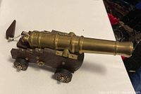 Photo showing brass barrel and wooden base of model cannon, wheels and fine detail visible.