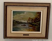 Framed oil painting titled 'Tranquility' showing a lake with a boat and trees, mounted on a beige mat board with a brown frame