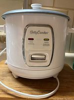 Front view of white Betty Crocker rice cooker showing Cook and Warm indicator lights, control switch, and power cord.