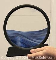 Close-up of blue sand art picture showing circular black frame, base, and flowing blue sand patterns inside clear glass.
