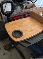 Photo of the seniors desk showing the wooden pivoting desktop with a built-in drink holder, black handle, and part of the black metal base.