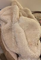 Three large cream-colored artificial sheepskin pieces with soft, fluffy texture placed on a chair and the floor, shown from above.