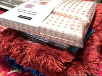 Close-up photo showing one beige/tan polka dot shower curtain in original packaging placed over red and cobalt blue fluffy bath mats.