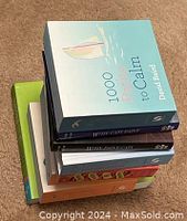Stack of 8 small, square paperback books with colorful covers, top one titled '1000 Petit to Calm' by David Blard
