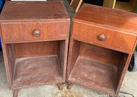 Photo of two identical solid wood bedside tables with dark stain, each with one drawer and open lower shelf, showing scratches and signs of wear.
