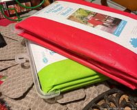 Photo showing folded red and green plastic tablecloths with flannel backing on beige fabric pot protectors.