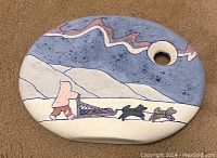 Top view of the flat oval ceramic vase showing painted Inuit with dog sled scene and a circular hole near one end