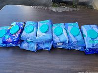 Seven Pampers baby wipes packages arranged in a row on a table, showing front design and resealable lids.