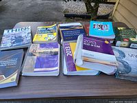 Wide view of books and manuals on table including Excel for Dummies, ICD-9-CM spiral manual, Think magazine, and others