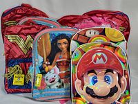 Front view of four new character bookbags arranged front and center showing Wonder Woman, Moana, Mario, and clear pink designs.
