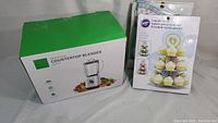 Photo of boxed KIDISLE countertop blender and Wilton cupcake stand packaging showing product details and branding.