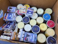 Box containing multiple glass jar candles and several packs of clamshell aromatherapy wax melts of various scent labels.